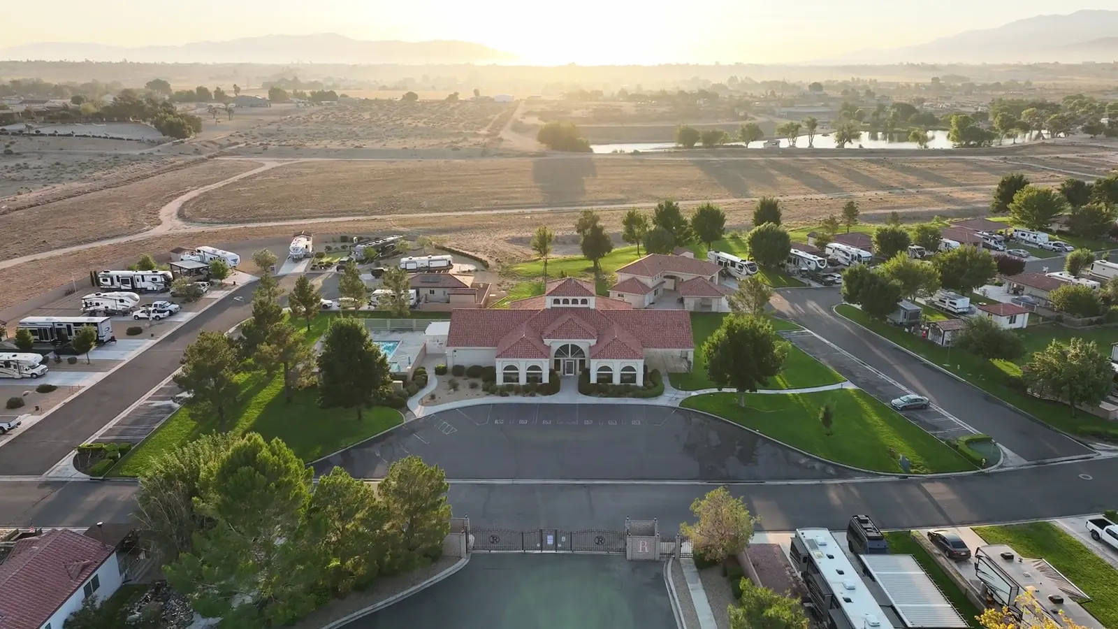 Aerial view at sunrise over a clubhouse, pool and parking area, from a drone flight.