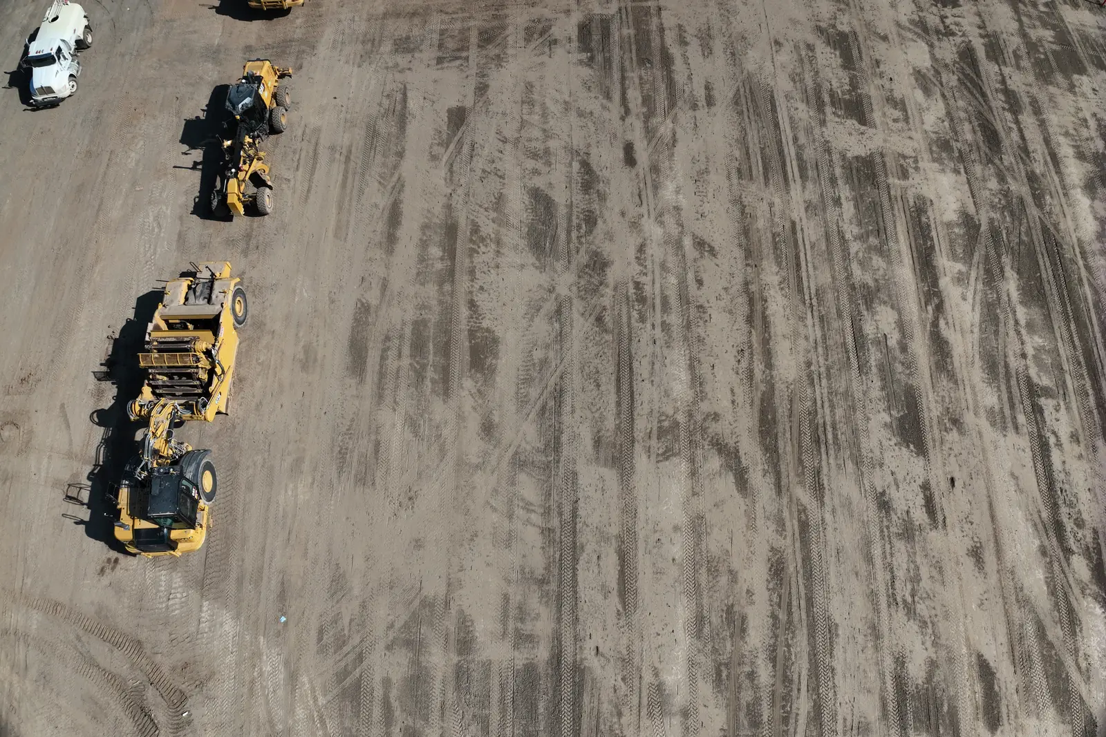 Graders and a loader lined up on a freshly graded construction pad, seen from above.