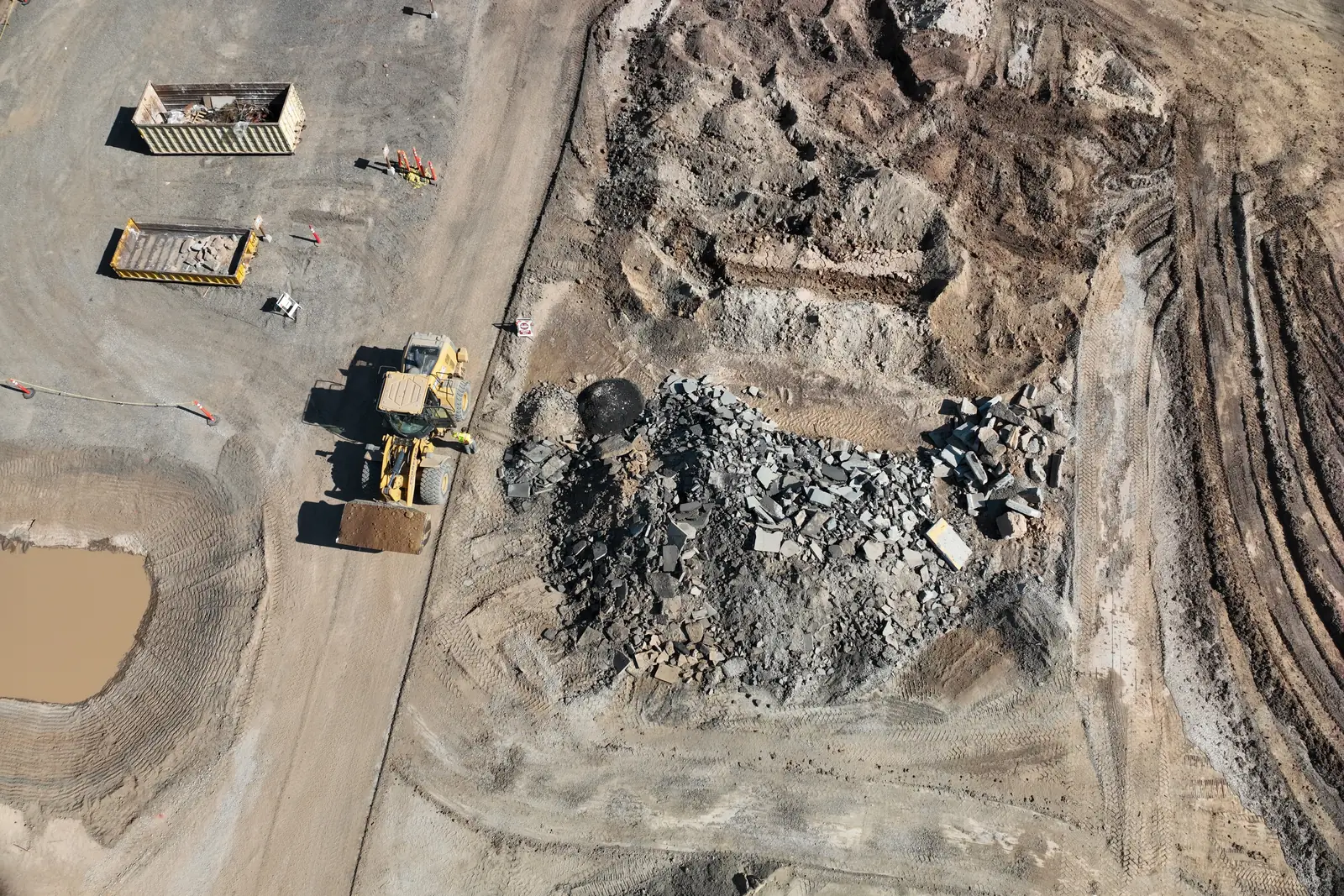 A demolition stockpile, a loader and roll-off bins on a construction site, seen from above.