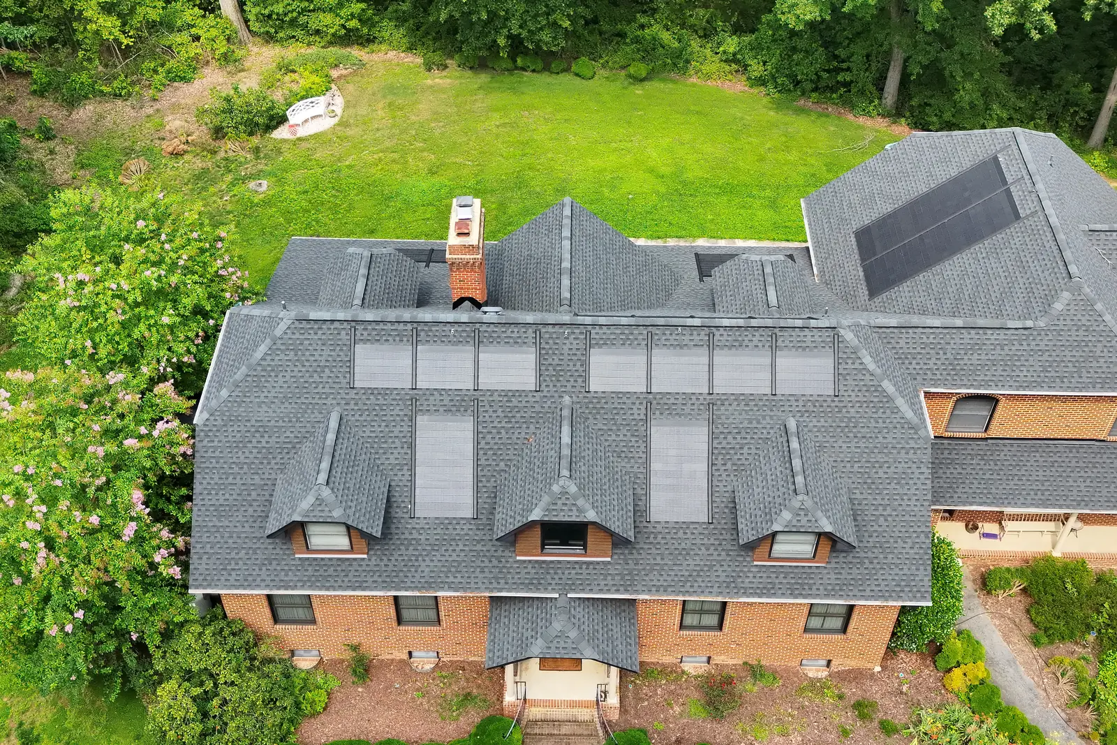 A brick house from the air, with a row of solar panels on one roof face and skylights on the other.