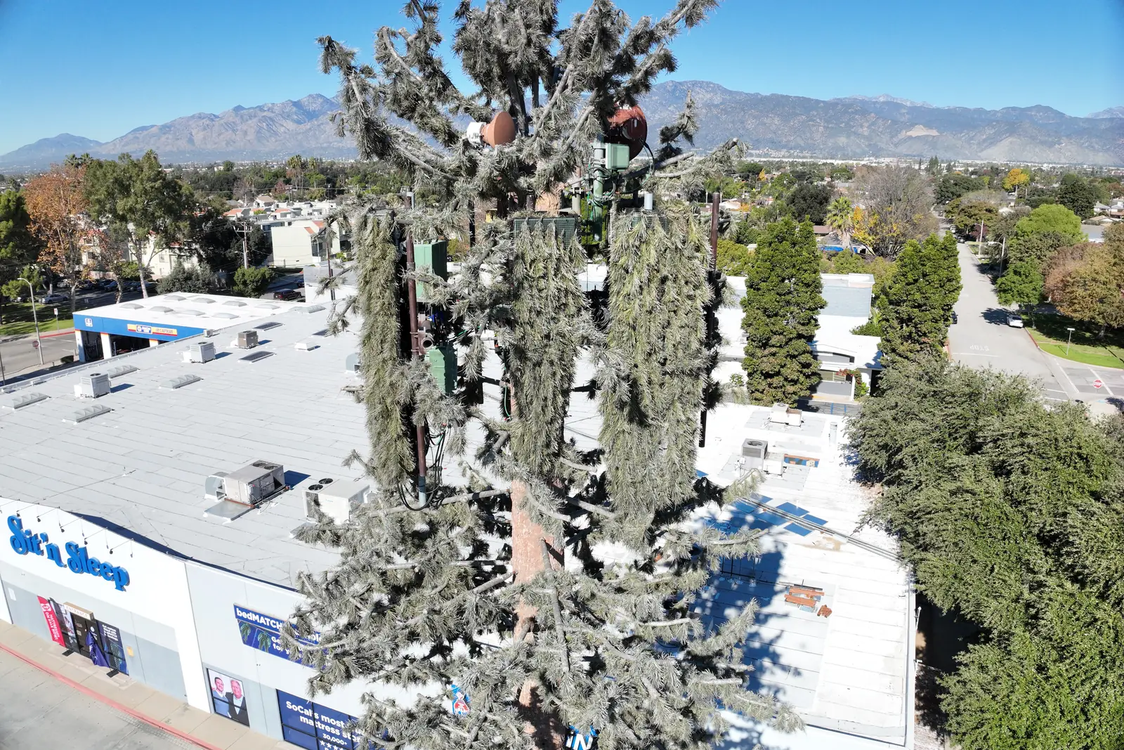 The same monopine tower from higher up, with the antenna arrays, the shopping-center roofs around it and the streets beyond.