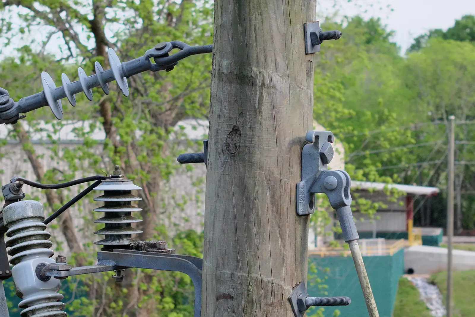 A close drone shot of a wooden pole: suspension insulators, a deadend clamp and lightning arresters on the crossarm.