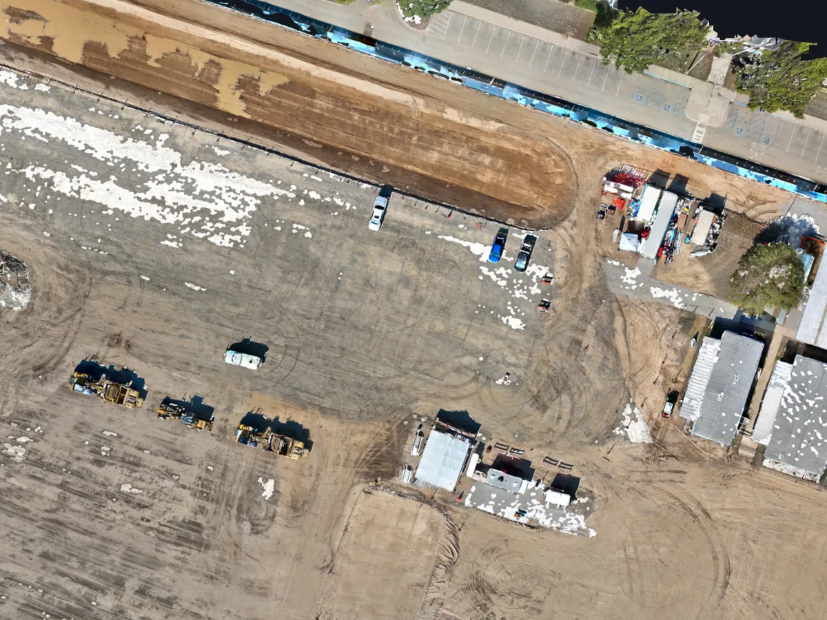 Close-up of the Costa Mesa orthomosaic: graded work pad with earthmovers, parked trucks, site trailers and buildings, sharp enough to pick out each vehicle.